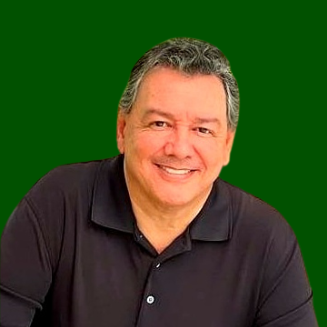 Un hombre sonriente con el pelo corto y gris que lleva un polo negro posa delante de un fondo verde sólido.