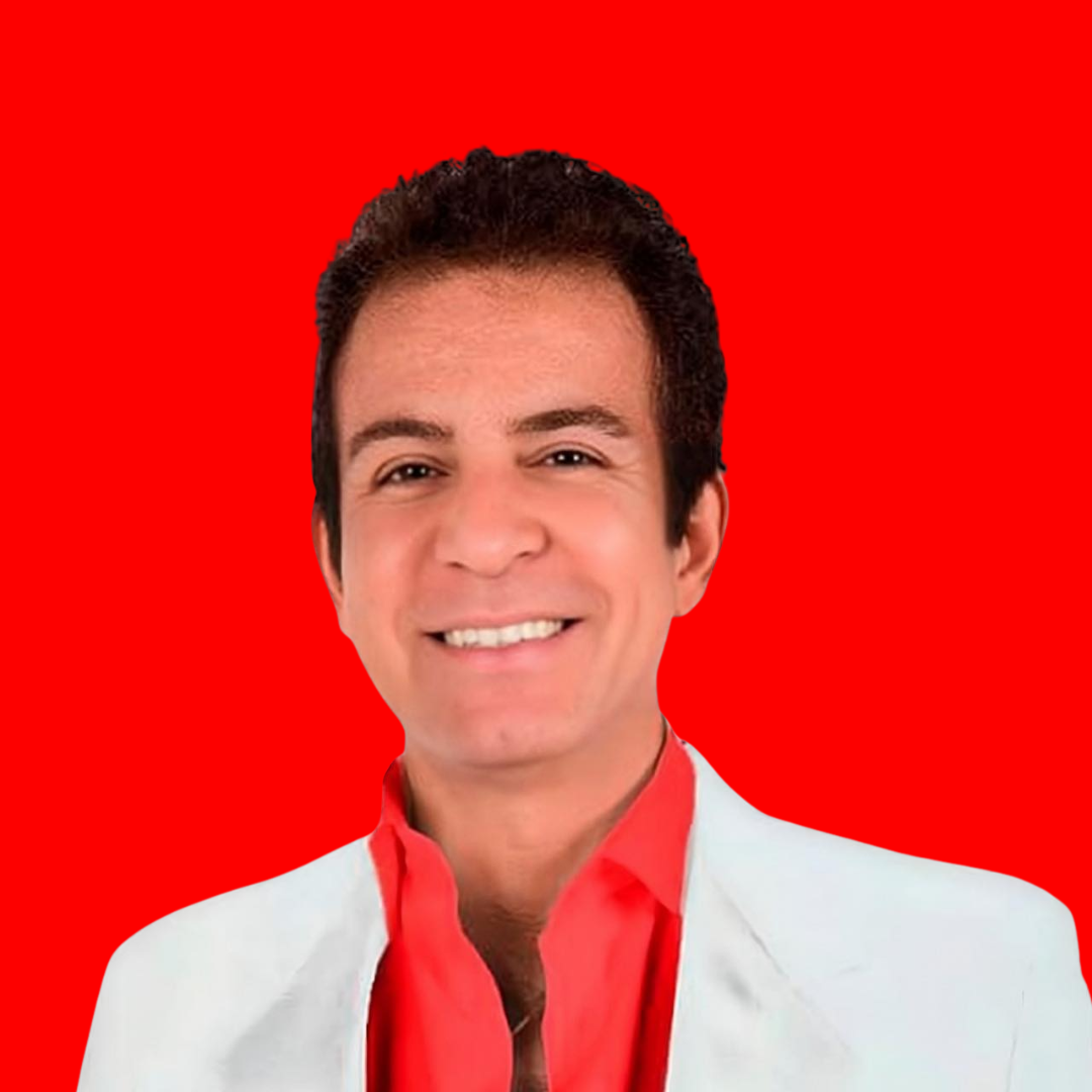 Un hombre sonriente con el pelo corto y oscuro lleva una chaqueta blanca sobre una camisa roja brillante, de pie delante de un fondo rojo sólido.
