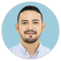 Retrato de un hombre con pelo corto oscuro, barba recortada y bigote, vestido con camisa de cuello azul claro, sonriendo ligeramente, con un fondo circular azul claro.