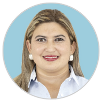 Una mujer de pelo largo castaño claro, con camisa de cuello azul claro y pendientes blancos, sonríe sobre un fondo azul claro.